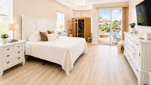 Une chambre à coucher comprenant un lit, des tables de chevet, une armoire, un ventilateur de plafond et donnant sur une piscine.