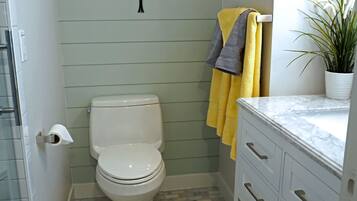 A bathroom with a toilet, a shower, a sink, and a decorative wall piece.