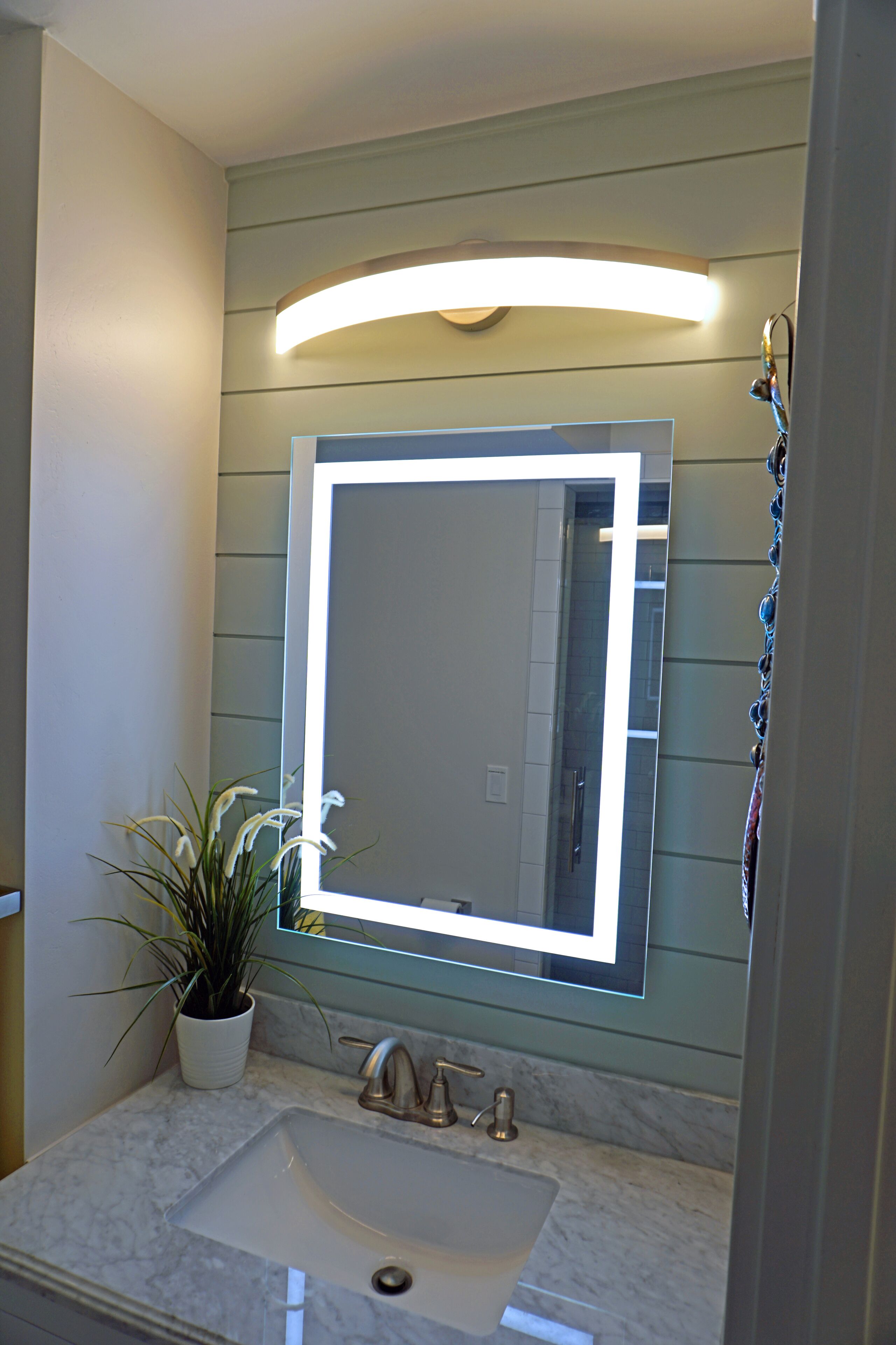 A bathroom with a large mirror, a sink, and a potted plant.