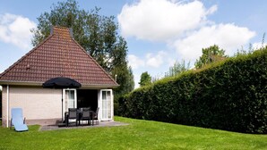A house with a tiled roof, a covered patio with a table and chairs, and a grassy yard with a wooden deck.