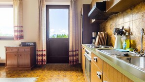 A kitchen with wooden cabinets, a stove, and a window with curtains. - Apartment in Mooswald in Carinthia With Pool (Fresach)