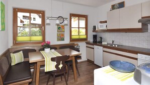 A compact kitchen with wooden cabinets, a built-in microwave, and a sink. There is a dining area with a bench and chairs, and large windows providing natural light. - Apartment With Panoramic Views in Fiss (Fiss)
