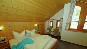 A wooden-paneled bedroom with a bed, two chairs, a nightstand, and a window with curtains. - Apartment With Panoramic Views in Fiss (Fiss)
