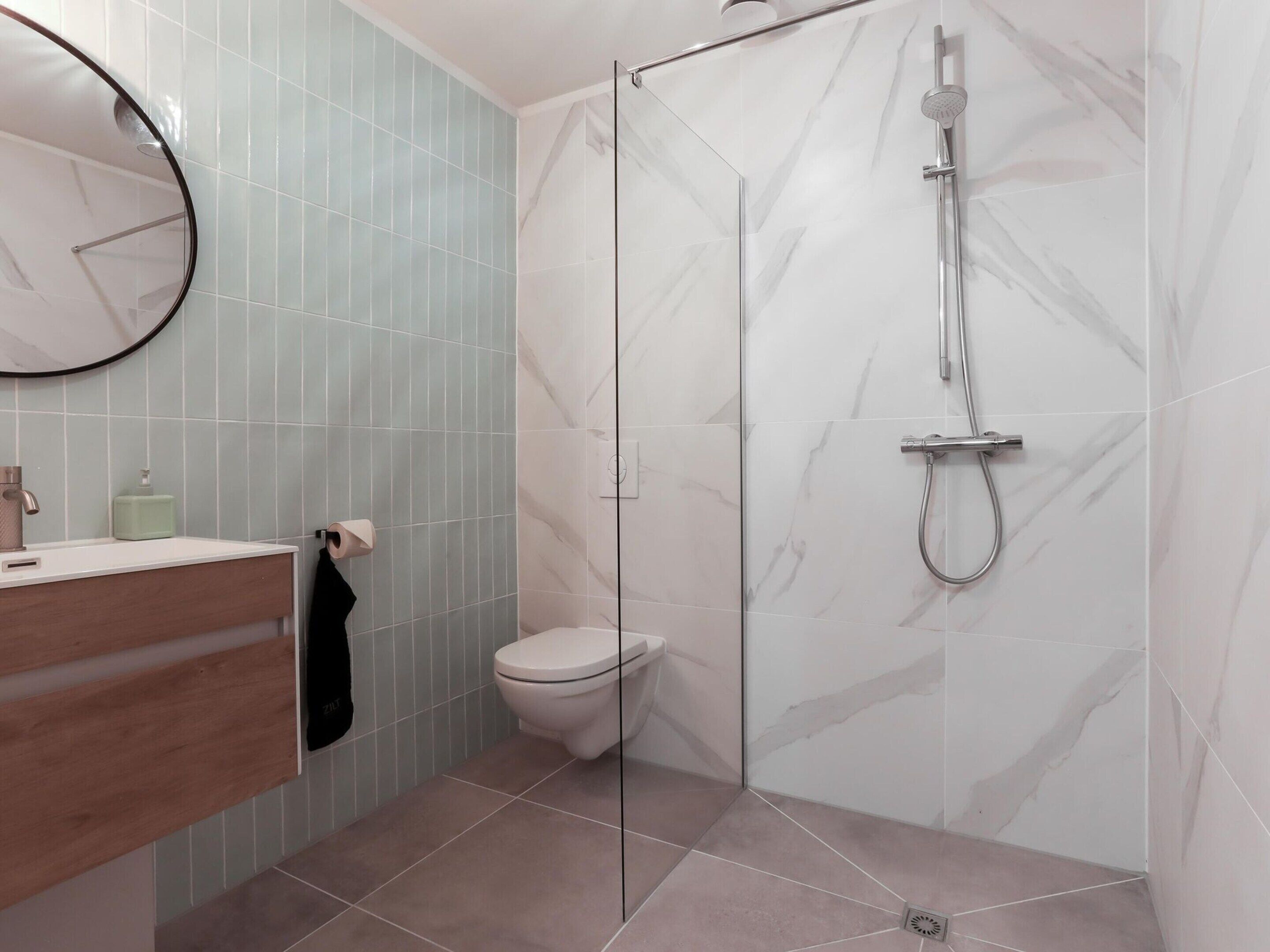 A modern bathroom with a glass-enclosed shower, a toilet, and a vanity with a mirror and soap dispenser.