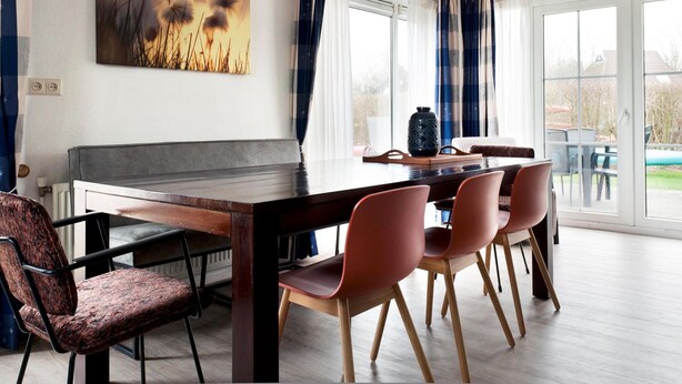 Un comedor moderno con una mesa de madera, sillas rojas y un ventanal con cortinas.