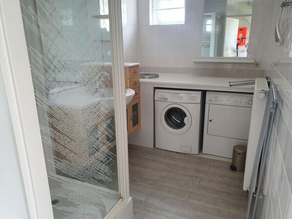 Une petite buanderie comprenant un lave-linge, un sèche-linge et un petit évier.