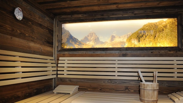A sauna with wooden walls, a large window with a mountain view, a wooden bucket, and a bench. - Chalet in ski Area in Wagrain With Sauna and Pool (Wagrain)