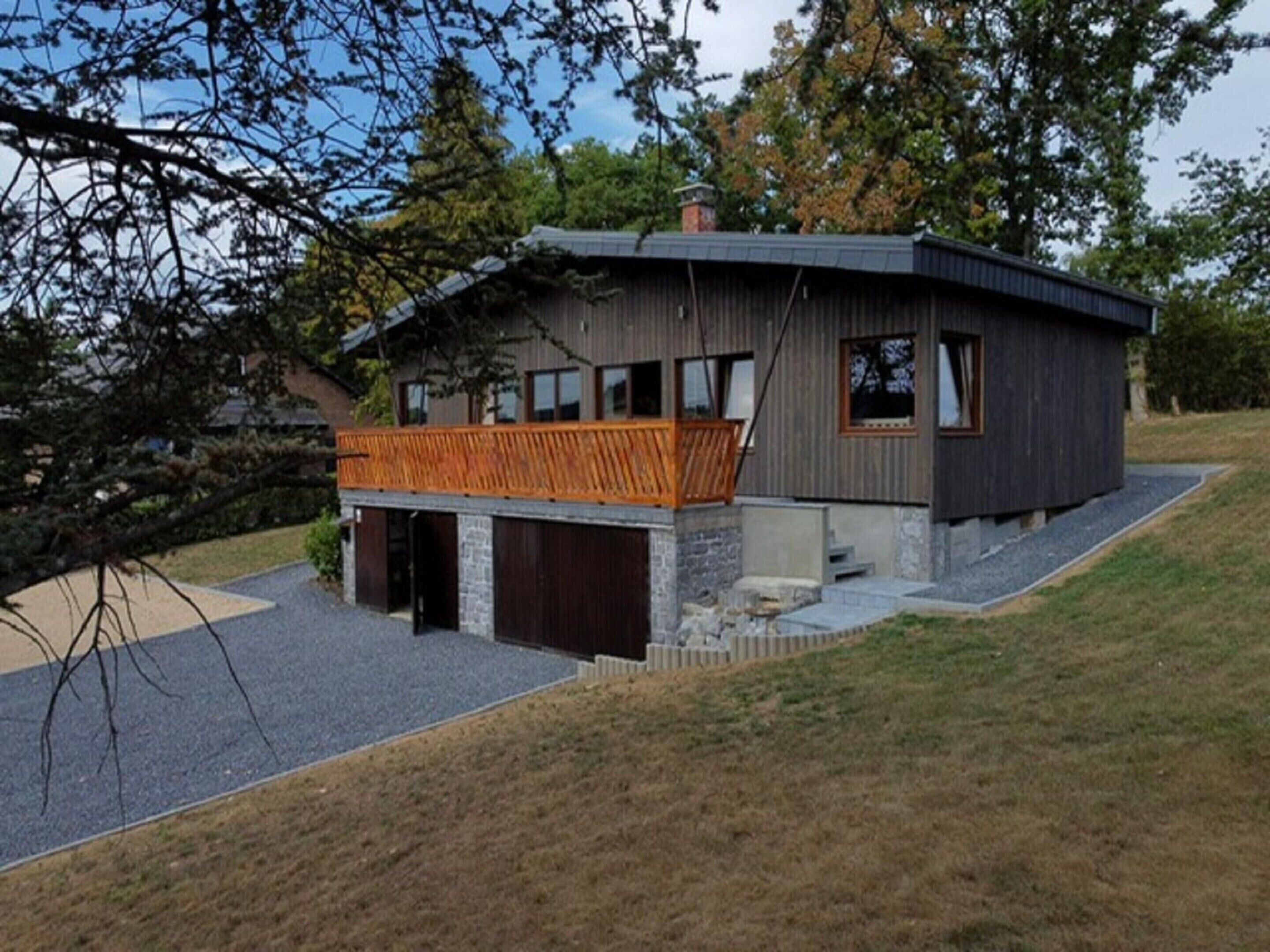 Ein modernes, zweistöckiges Haus mit Holzterrasse, Stein Fundament und Garage.