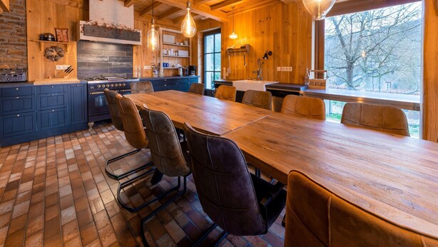 A spacious kitchen with a large wooden table and chairs, a built-in oven, and hanging light fixtures. - Gite in Belgium Near Scenic Hiking Trails (Vresse-sur-Semois)