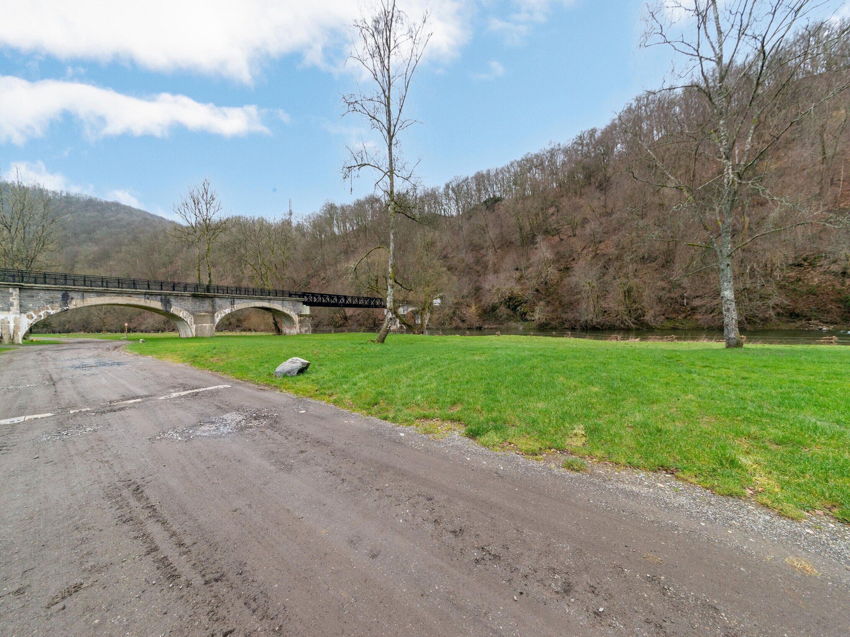 A stone bridge over a river with a grassy field and trees in the background.