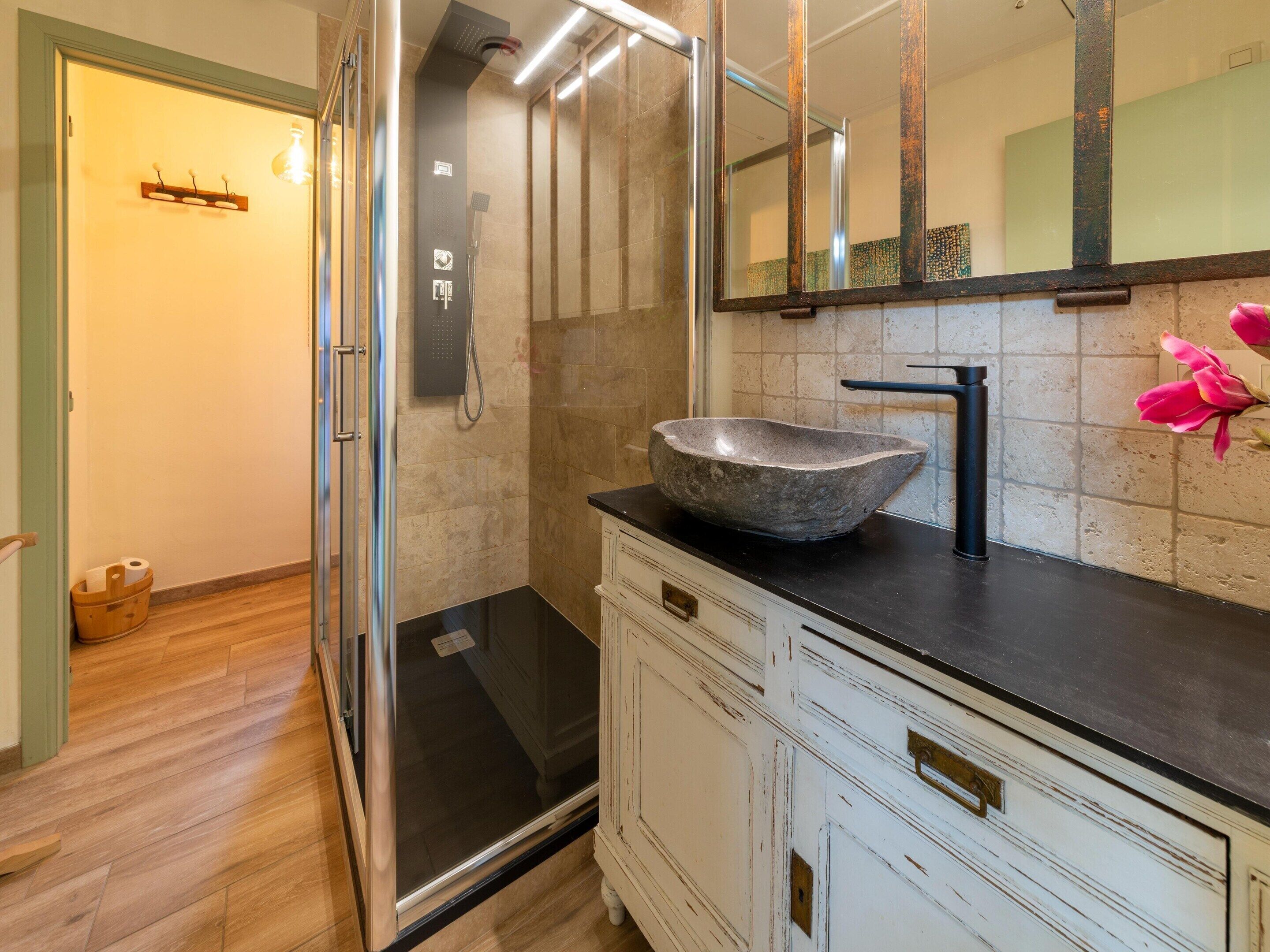 Un bagno con lavabo in pietra, uno specchio grande e cabina doccia.