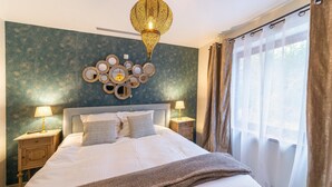 A neatly made bed with a fluffy blanket, two bedside tables with lamps, a decorative wall piece, and a large window with curtains. - Gite in Belgium Near Scenic Hiking Trails (Vresse-sur-Semois)