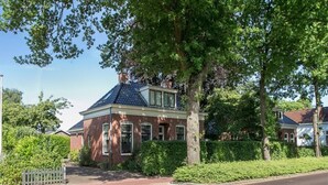A brick house with a gabled roof, surrounded by greenery and a white picket fence. - Shared Garden Apartment Retreat (Vrouwenpolder)