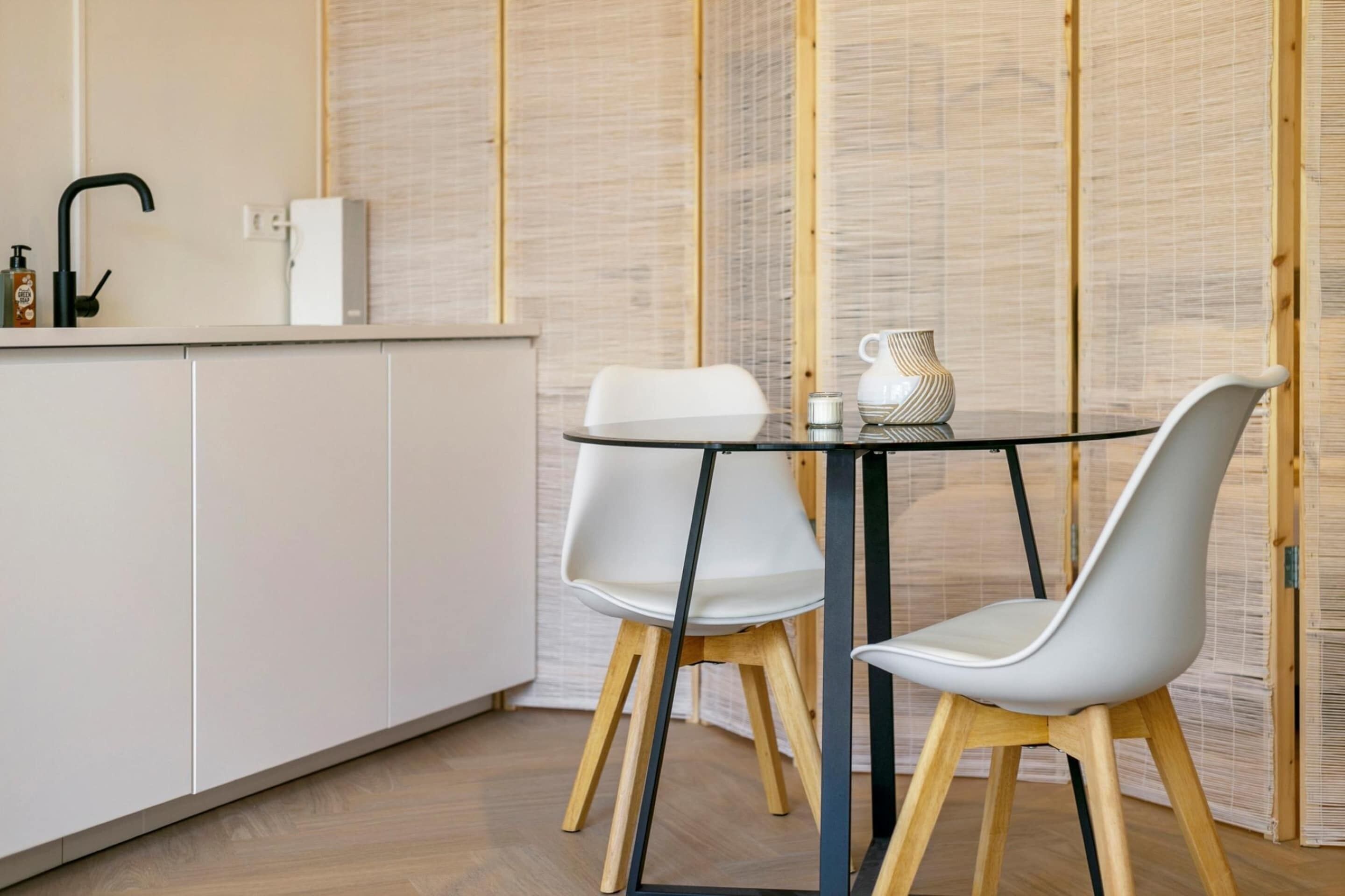 A modern kitchen with white cabinets, a black faucet, and a round table with two white chairs.