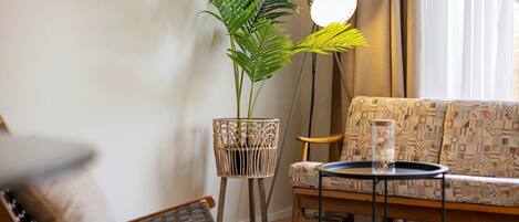 En stue med en stribet sofa, en træstol, et lille bord med et glas, en gulvlampe og en potteplante.