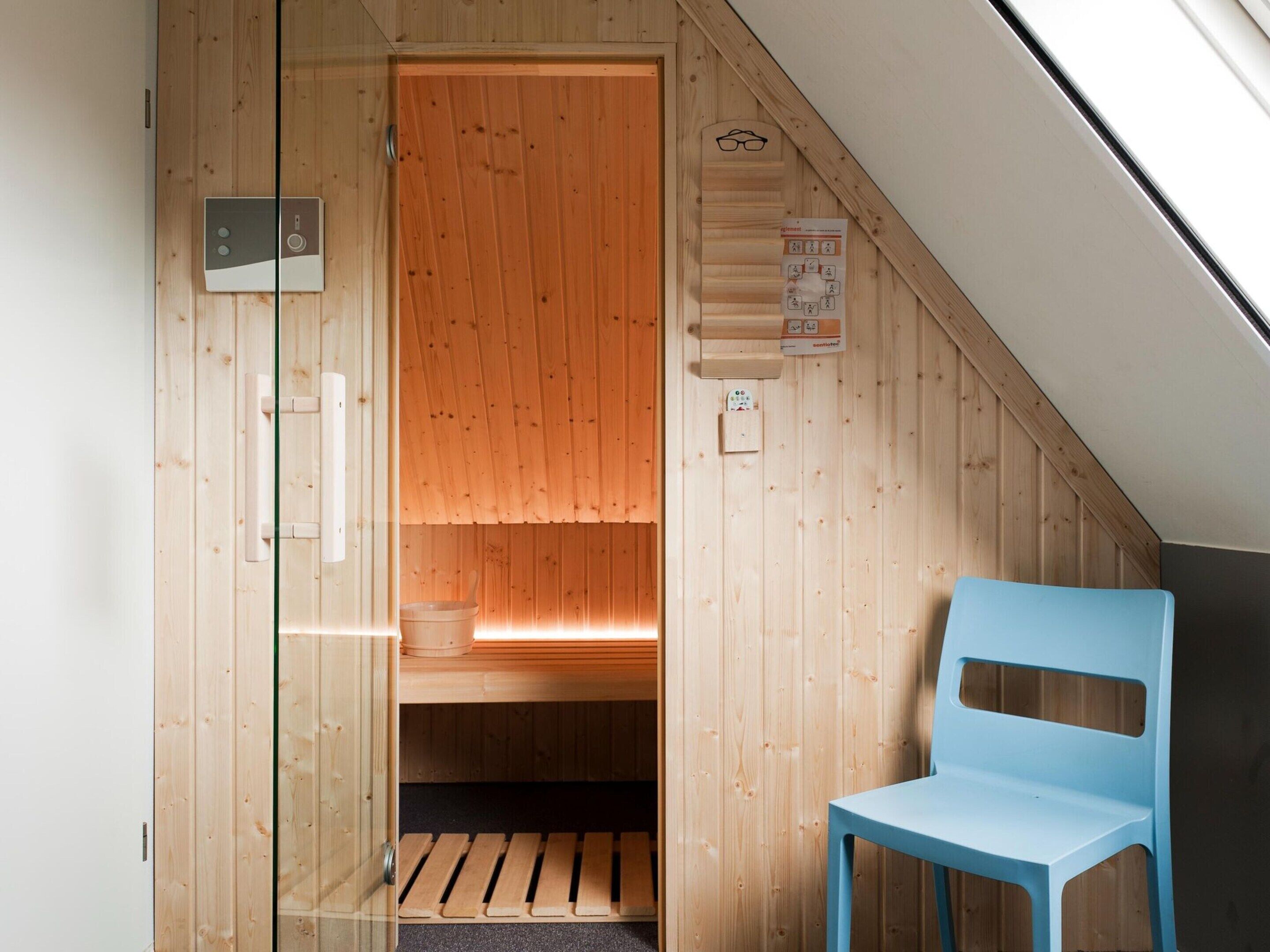 Une cabine de sauna en bois, avec un banc, une chaise bleue et un panneau de commande de sauna.