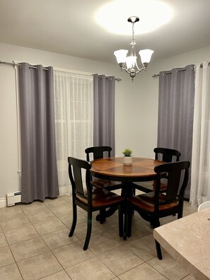Enjoy meals in this cozy dining area with a round table and four chairs, a potted plant, and a chandelier.