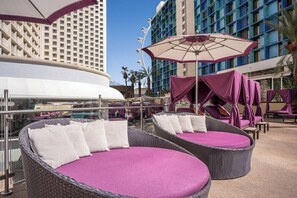 A rooftop lounge area with wicker lounge chairs and purple cushions, a glass balustrade, and a view of a high-rise building. - Queen Room at a  Hotel (Las Vegas)