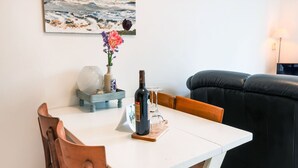 Ein Essbereich mit einem weißen Tisch, Holzsesseln, einer Blumenvase, einer Flasche und einem Kerzenständer.