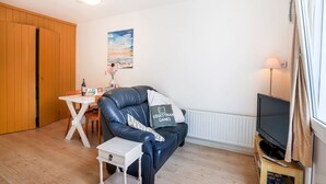 Ein gemütliches Wohnzimmer mit einer Ledersofa, einem kleinen weißen Tisch, einem Fernseher auf einem Holzschrank und einem Bild an der Wand.