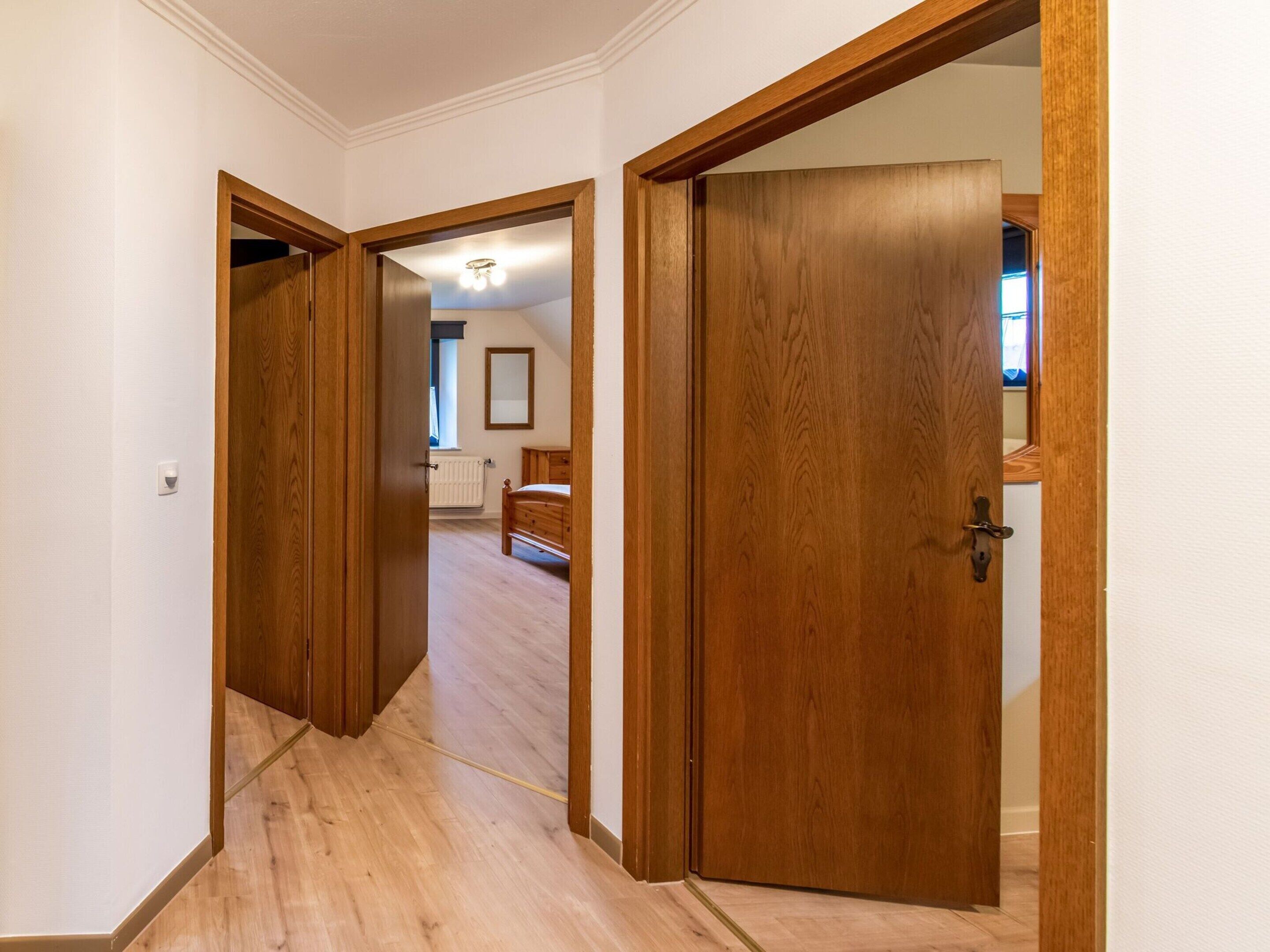 A hallway with wooden doors leading to a bedroom with a bed and a window.