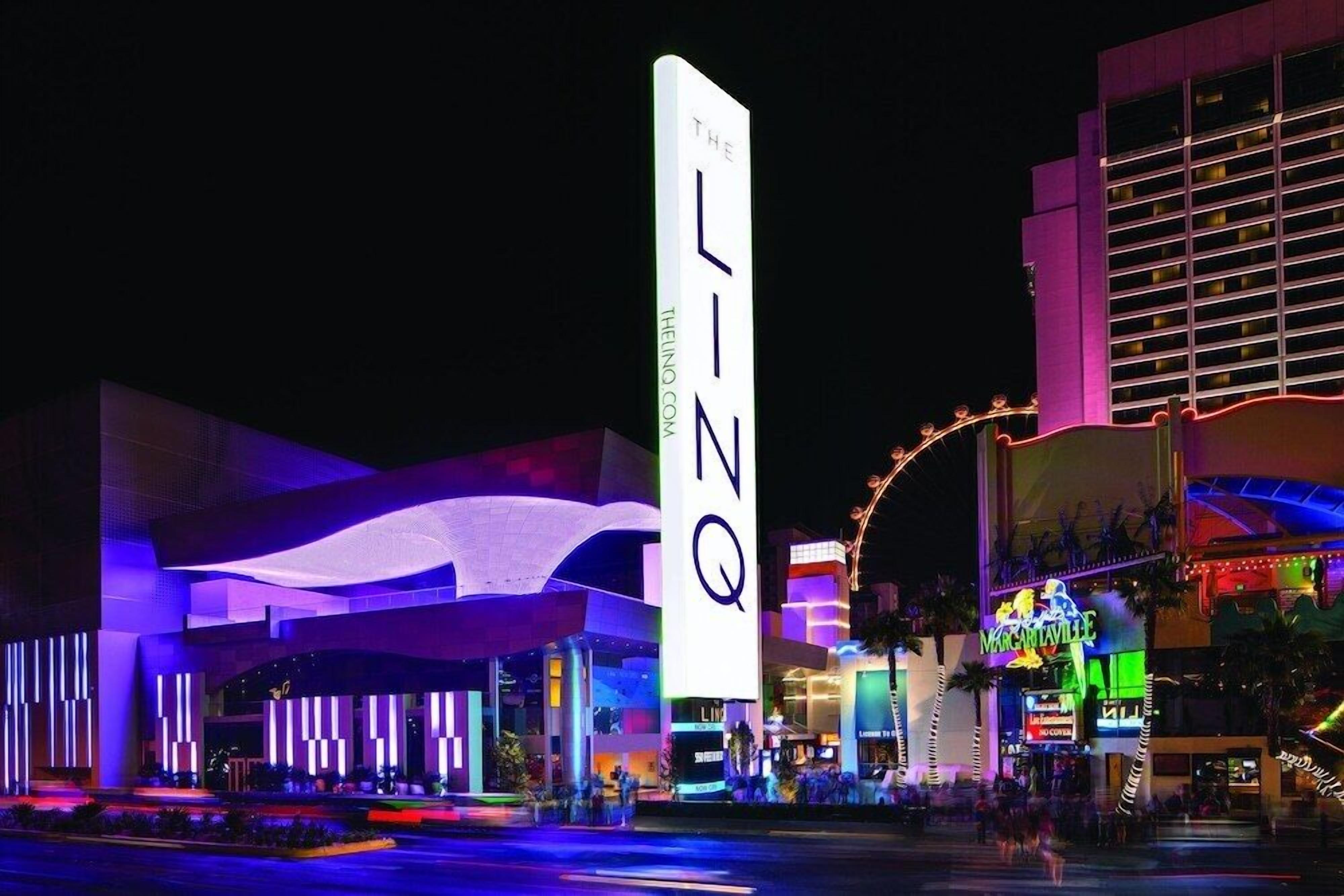 Eine hell erleuchtete Hotelfassade mit einer auffälligen, vertikalen Signage, einer gewölbten Dachkonstruktion und einem in der Nähe gelegenen Casino mit Neonreklame.