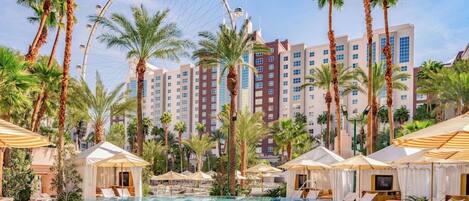 A hotel pool area with a Ferris wheel, palm trees, and a large building in the background.