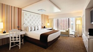A hotel room with a large bed, a desk, a chair, a TV, and a window with blinds. - Room with One Bed at a  Hotel (Las Vegas)