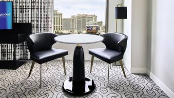 A hotel room with a round table and two chairs, a TV, a patterned carpet, and a view of a casino building.