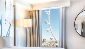 Een hotelkamer met een groot raam, een bed, een lamp en uitzicht op een reuzenrad.