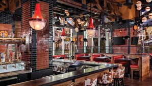 Ein Restaurant mit Ziegelwänden, roten Sitzelementen und hängenden, kugelförmigen Lampen.