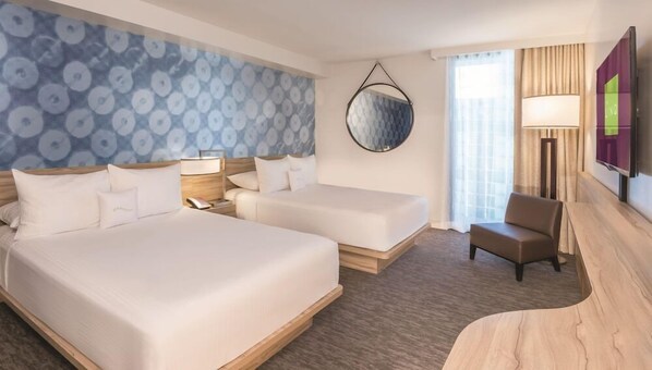 A hotel room with two beds, a desk, a chair, a round mirror, and a TV.