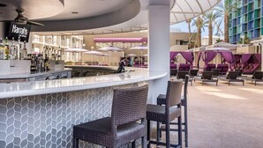 A modern bar area with a curved ceiling, a bar counter, and seating with umbrellas. - King Room at a  Hotel (Las Vegas)