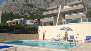 A modern building with a pool area, including lounge chairs and a sun umbrella. - Beach Holiday Home in Makarska (Makarska)