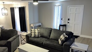 A living room with a grey sofa, two matching armchairs, a white coffee table, and a white side table. There is a ceiling fan, a light fixture, and a door in the background. - Newly Remodeled, Cozy & Private Condo - Beautiful Fountain Hills - Near Fountain (Fountain Hills)