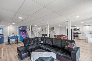 Uma sala de estar ampla com sofá seccional, mesa de pebolim e escada para o segundo andar.