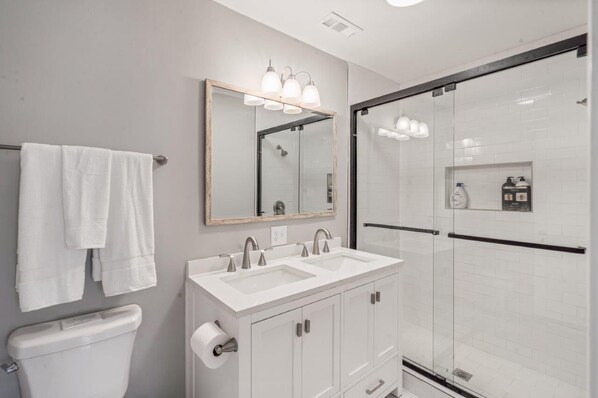 A modern bathroom with a double sink vanity, a large mirror, and a glass shower enclosure.