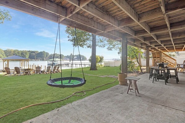 Um alpendre coberto com balanço, assentos externos e vista para um lago.