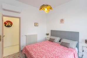 Quarto com cama, radiador, porta e luminária fixada na parede.