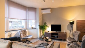 Uma sala de estar moderna com um sofá, cadeiras, uma televisão e uma planta.
