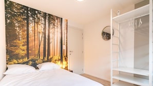 Quarto com cama, guarda-roupa e um mural na parede com tema de floresta.
