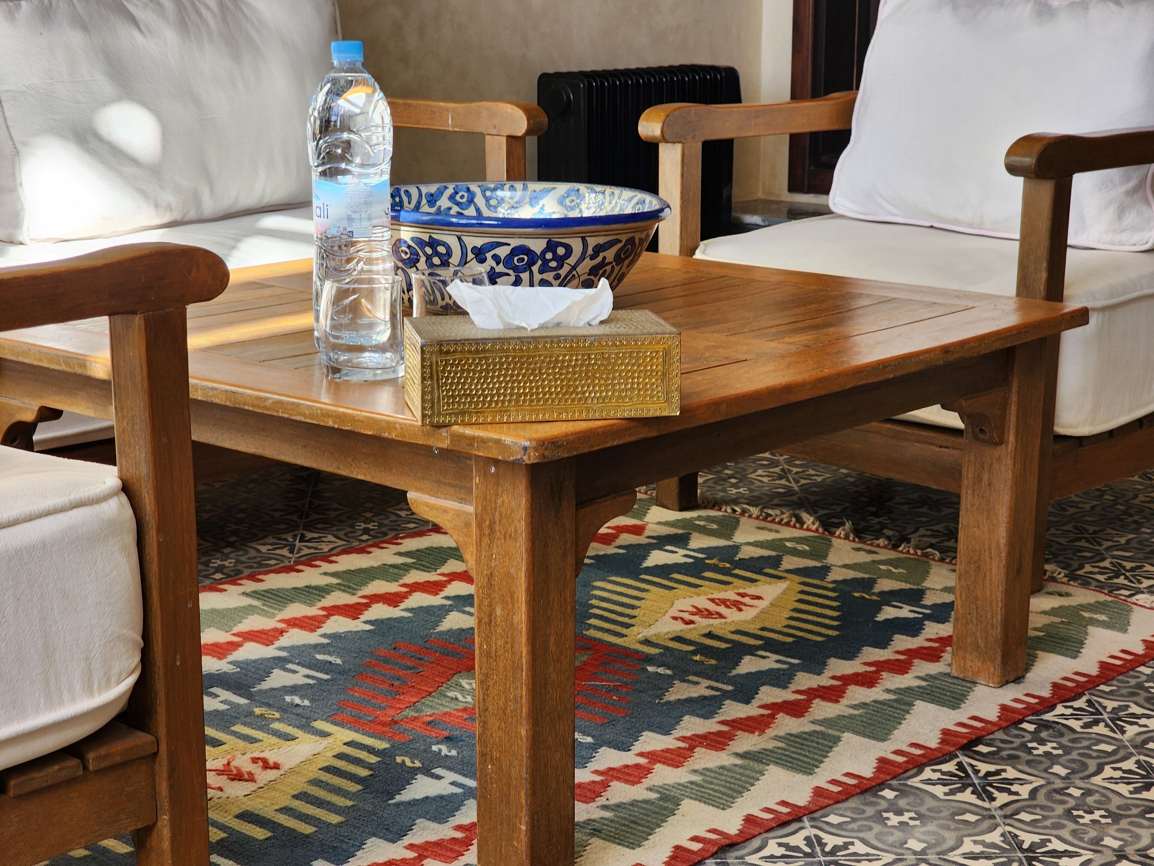 A wooden table with a blue and white bowl, a clear water bottle, and a tissue box.