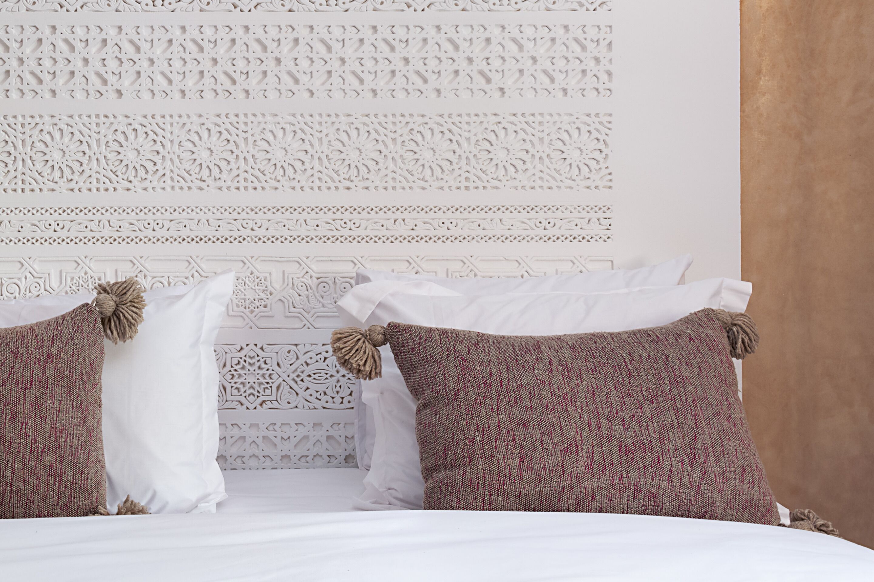 Una cama con almohadas blancas y marrones, un cabecero decorativo y una pared con textura.
