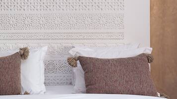 Una cama con almohadas blancas y marrones, un cabecero decorativo y una pared con textura.