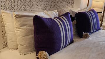 Een bed met witte en paarse kussens, een decoratief hoofdbord en een lamp.