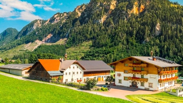 Un chalet de montagne composé d’un grand bâtiment en bois, d’un bâtiment plus petit, peint en blanc, et d’un restaurant doté d’une terrasse.