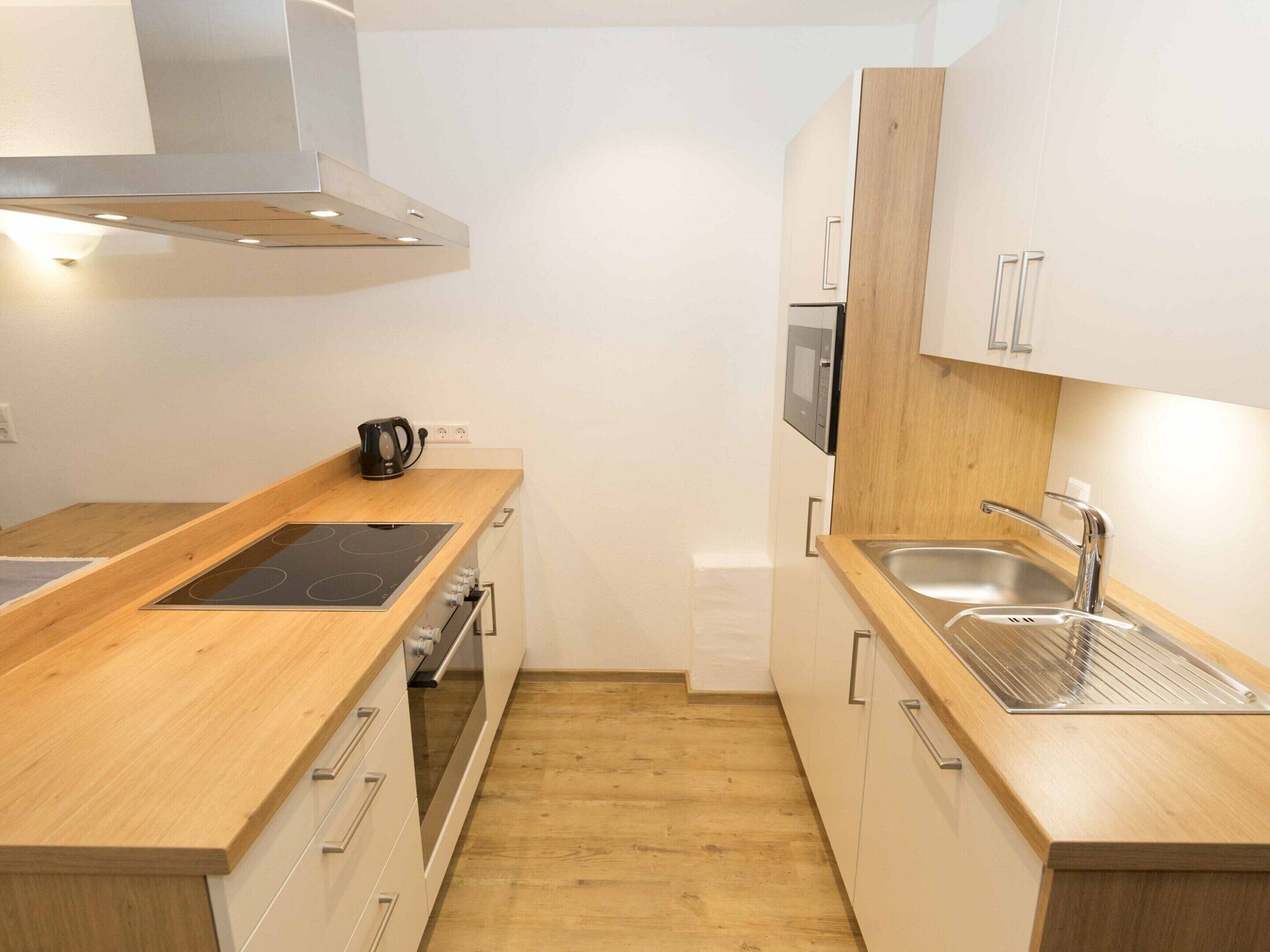 A compact kitchen with wooden countertops, a built-in oven, a stainless steel sink, and a microwave.