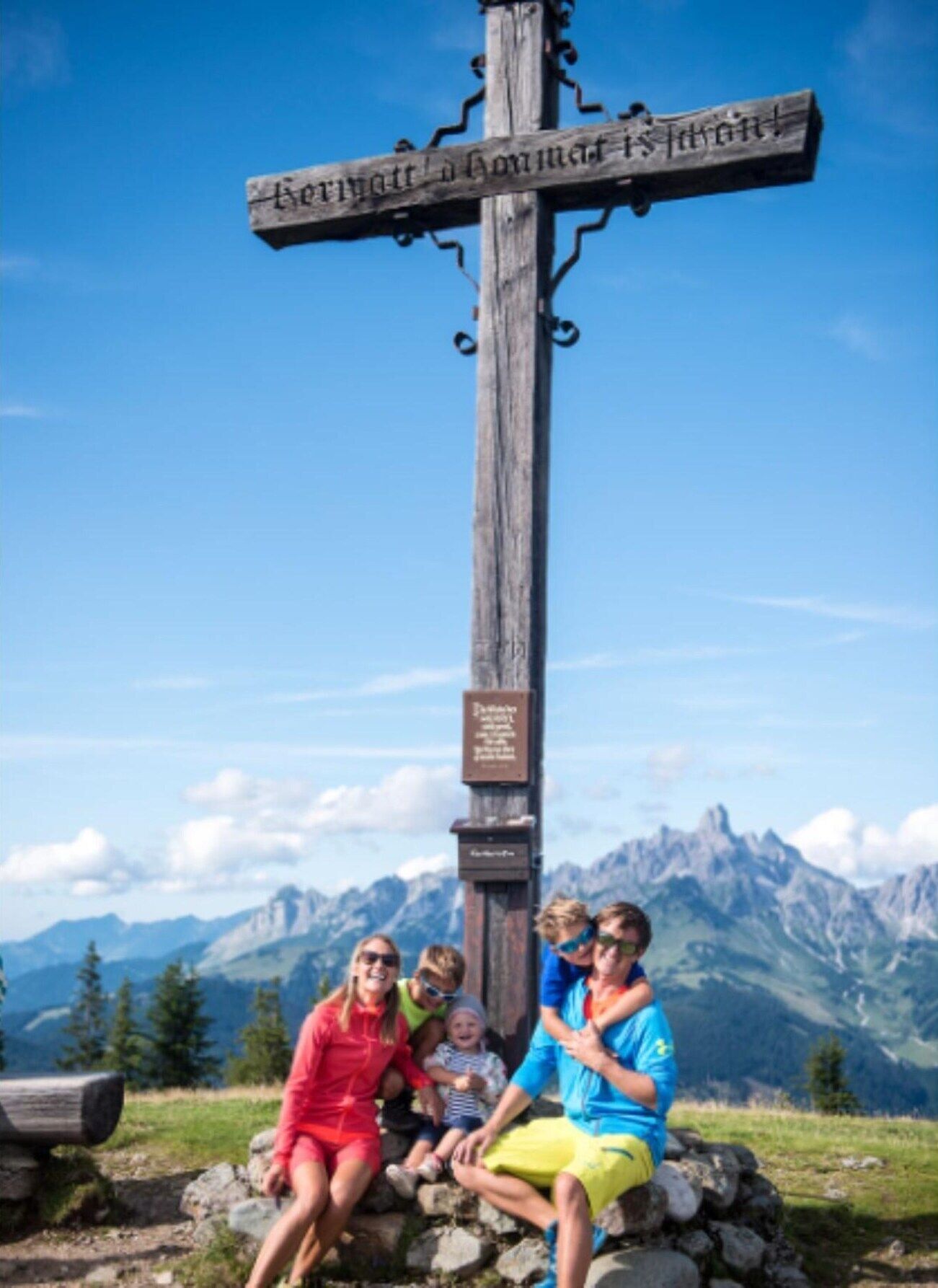 A wooden signpost with inscriptions, set against a mountainous backdrop.