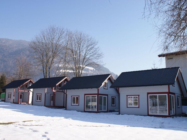 A row of white houses with red trim and dark roofs, set against a snowy landscape with mountains in the background. - Holiday Home Bodensdorf Near Gerlitzen Ski Area (Steindorf am Ossiacher See)