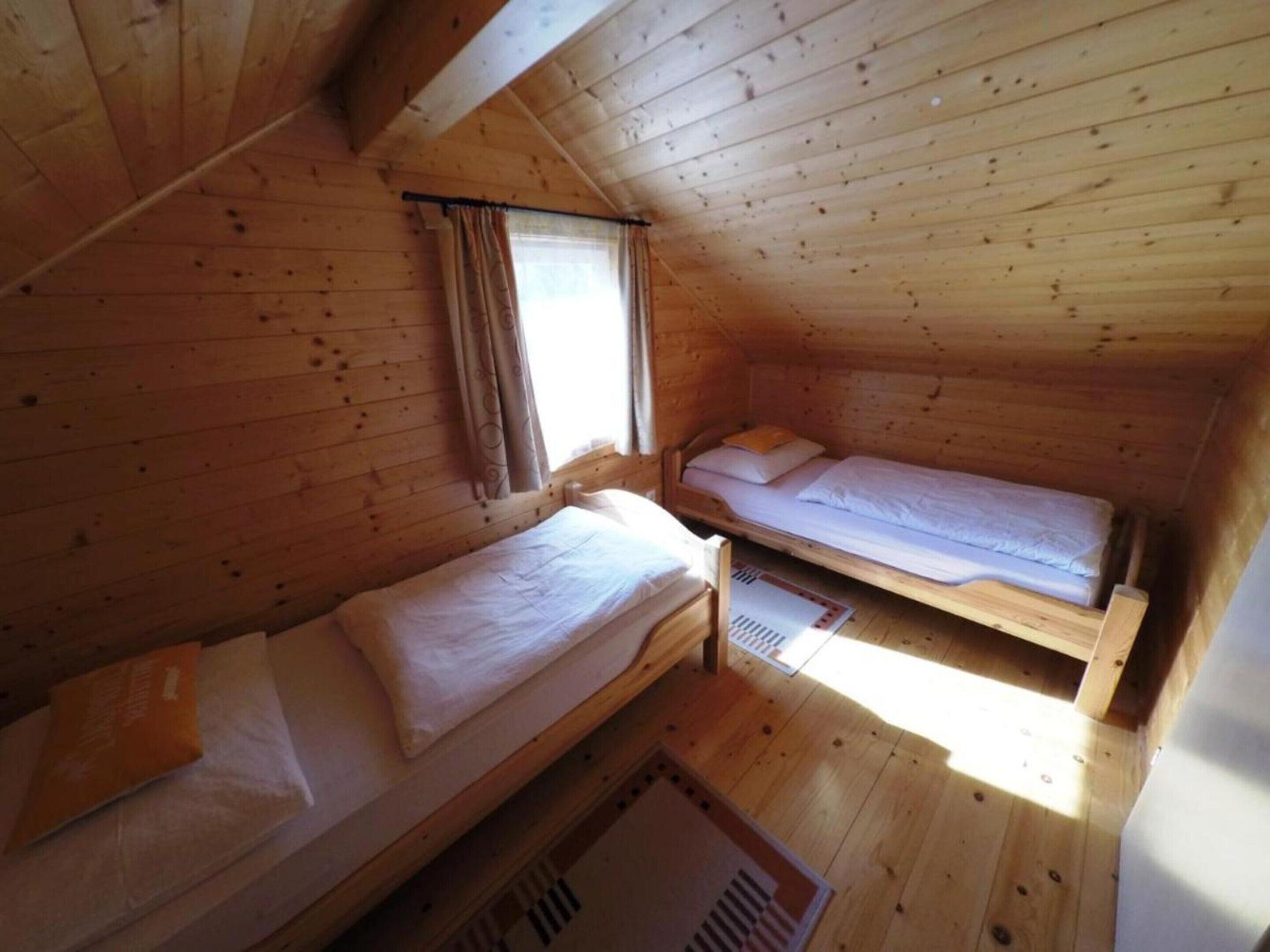 Une cabine équipée de deux lits superposés en bois, d’une fenêtre avec des rideaux et d’un plafond en pente.